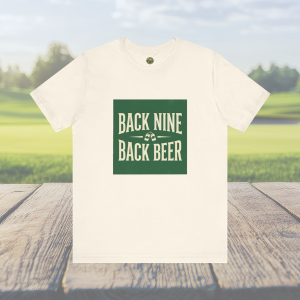 White t-shirt with 'Back Nine Back Beer' text on a wooden surface with a blurred green field and blue sky in the background