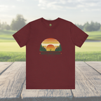 Maroon t-shirt with a sunset and tree graphic on a wooden surface with a natural background