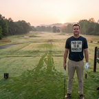 Man on a golf course holding a golf club with a sunset in the background